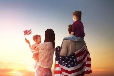 Patriotic holiday. Happy family, parents and daughters children girls with American flag outdoors. USA celebrate 4th of July.
