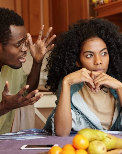 People and relationships concept. African American couple arguing in kitchen: man in glasses gesturing in anger and despair, screaming at his beautiful unhappy girlfriend who is totally ignoring him