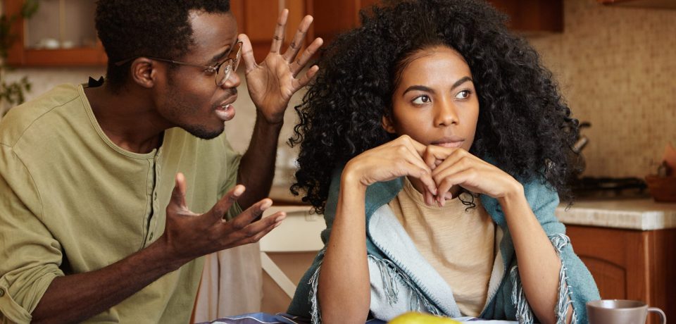 People and relationships concept. African American couple arguing in kitchen: man in glasses gesturing in anger and despair, screaming at his beautiful unhappy girlfriend who is totally ignoring him