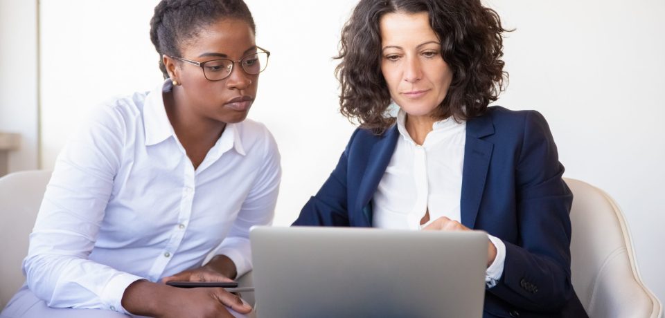 Serious businesswomen watching presentation together. Business women sitting in armchairs, using laptop, looking at screen. Teamwork concept